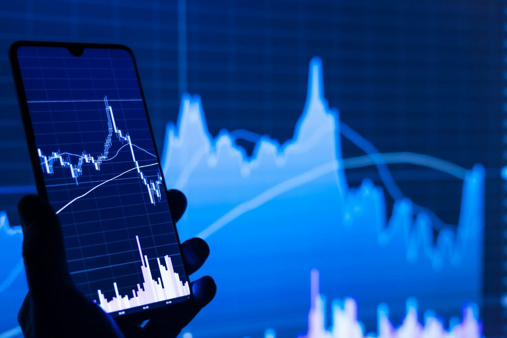 Trader holding a phone showing a live chart